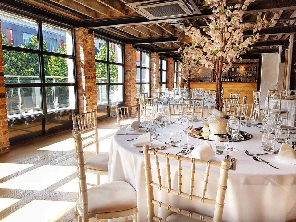 Tables set for a wedding with floor to ceiling windows and a bar in the background